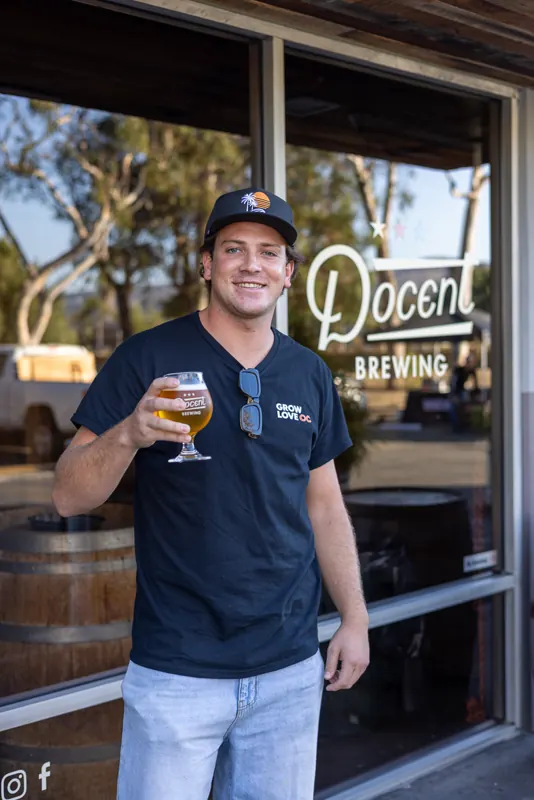 A man in a Docent Brewing shirt holding a beer at the Docent door.